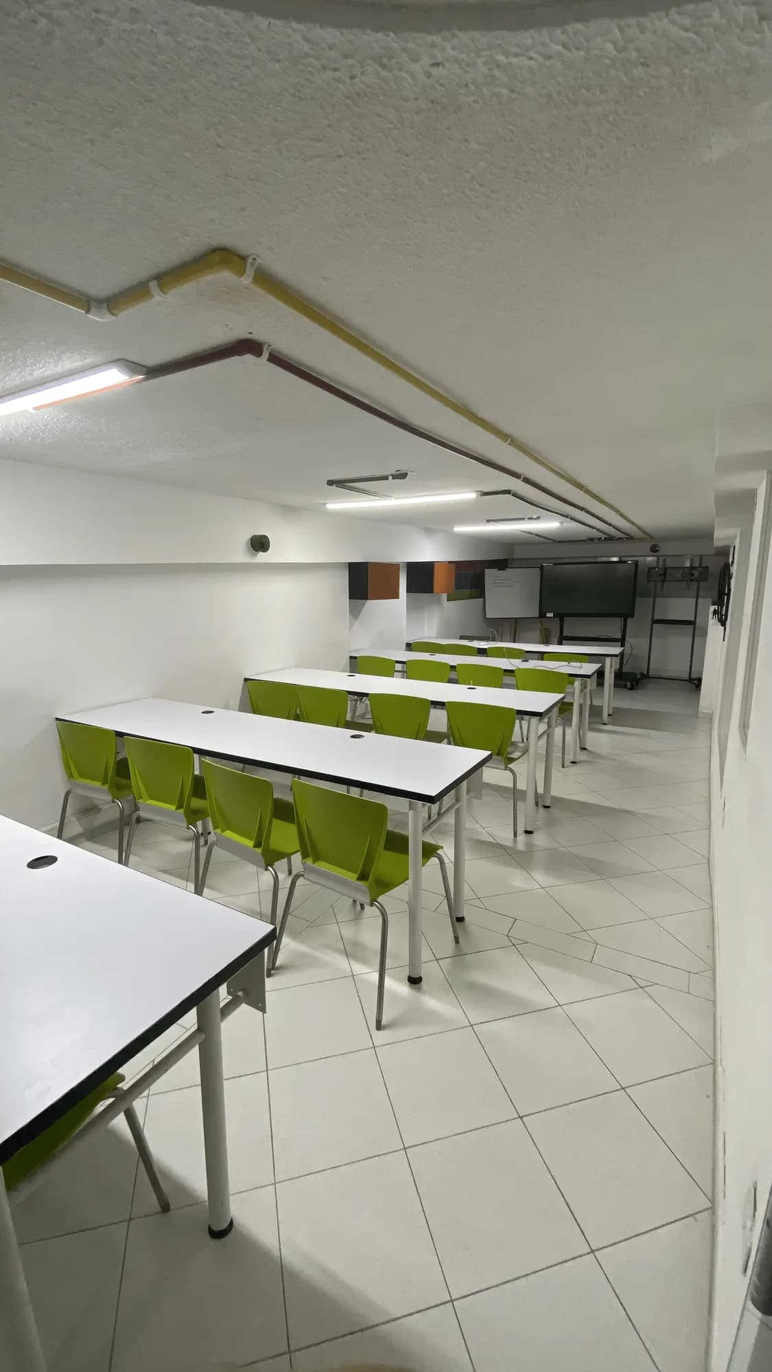 Sala de capacitación con mesas en filas y sillas verdes